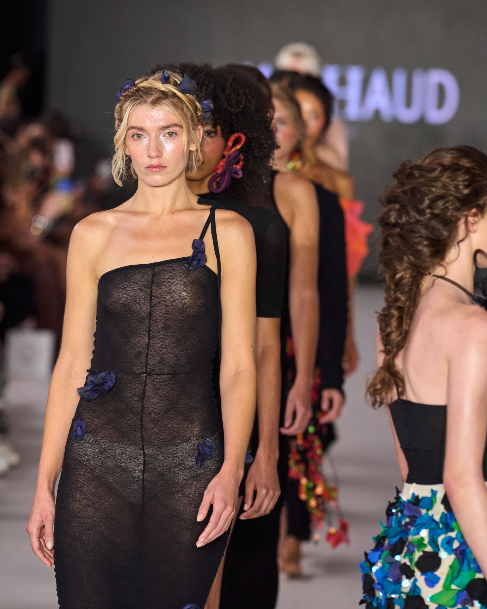 A model walking the runway wearing a sheer black dress.