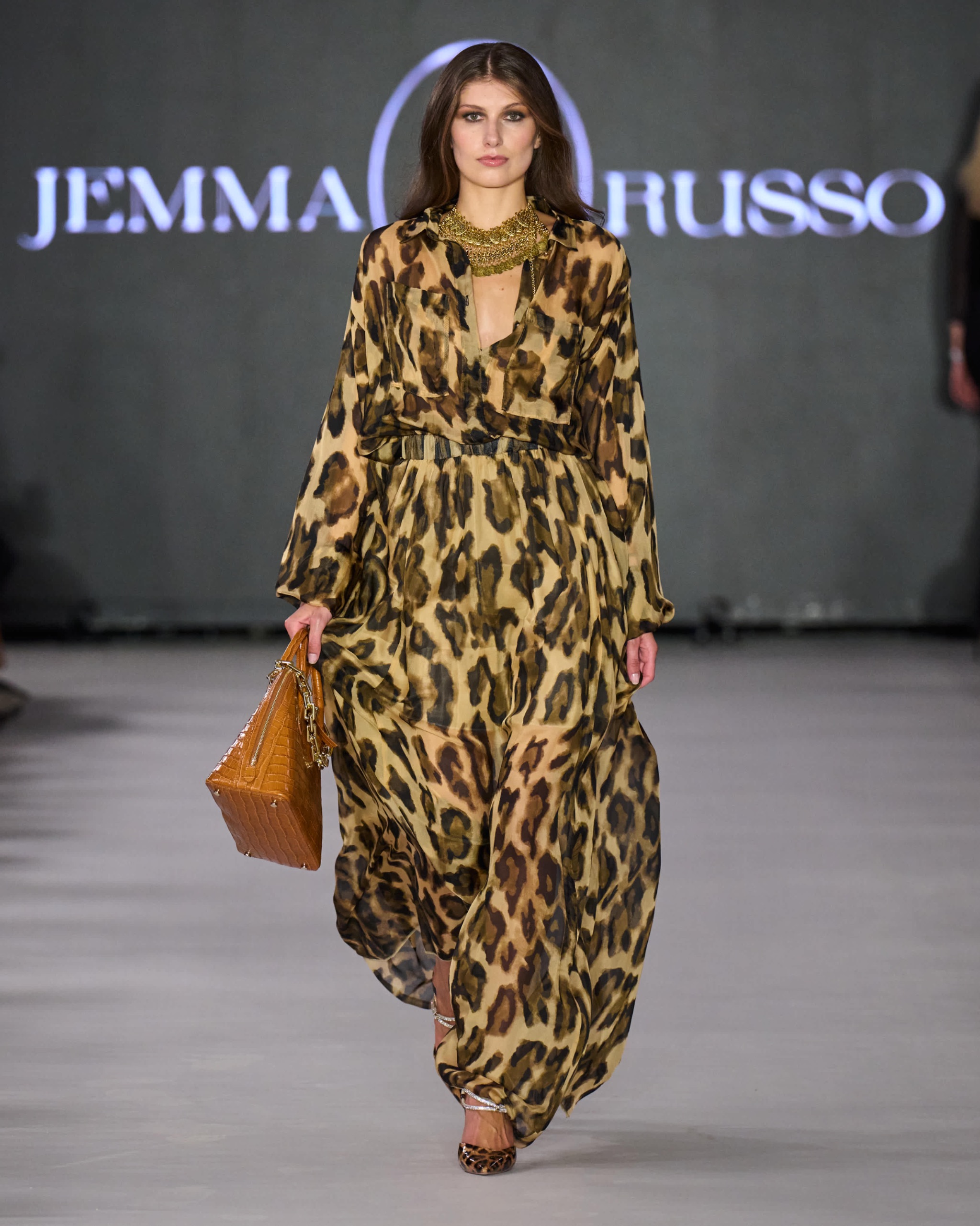 A model walking the runway wearing a long sleeved leopard print dress.