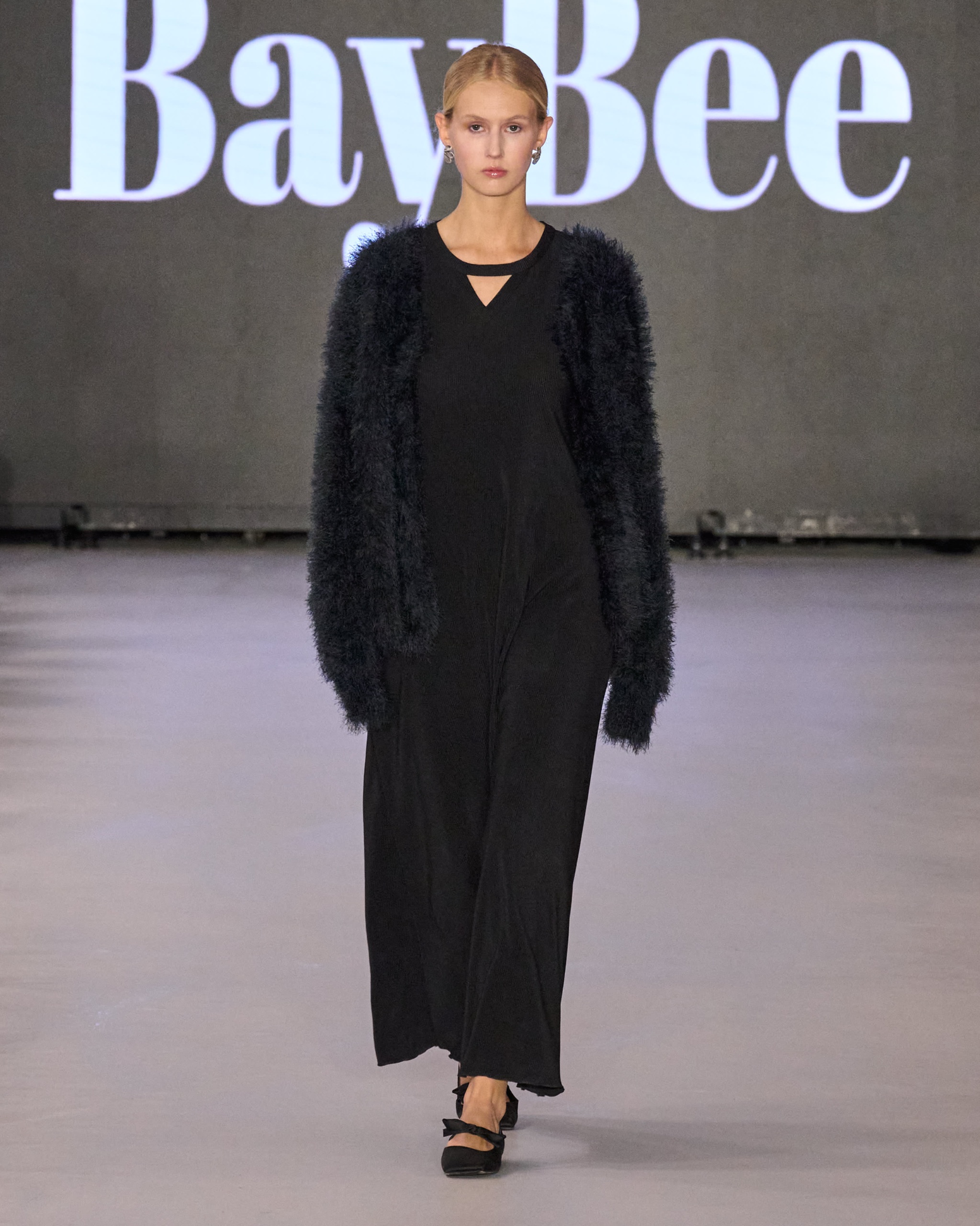 A model walking the runway wearing a long-sleeved black dress.