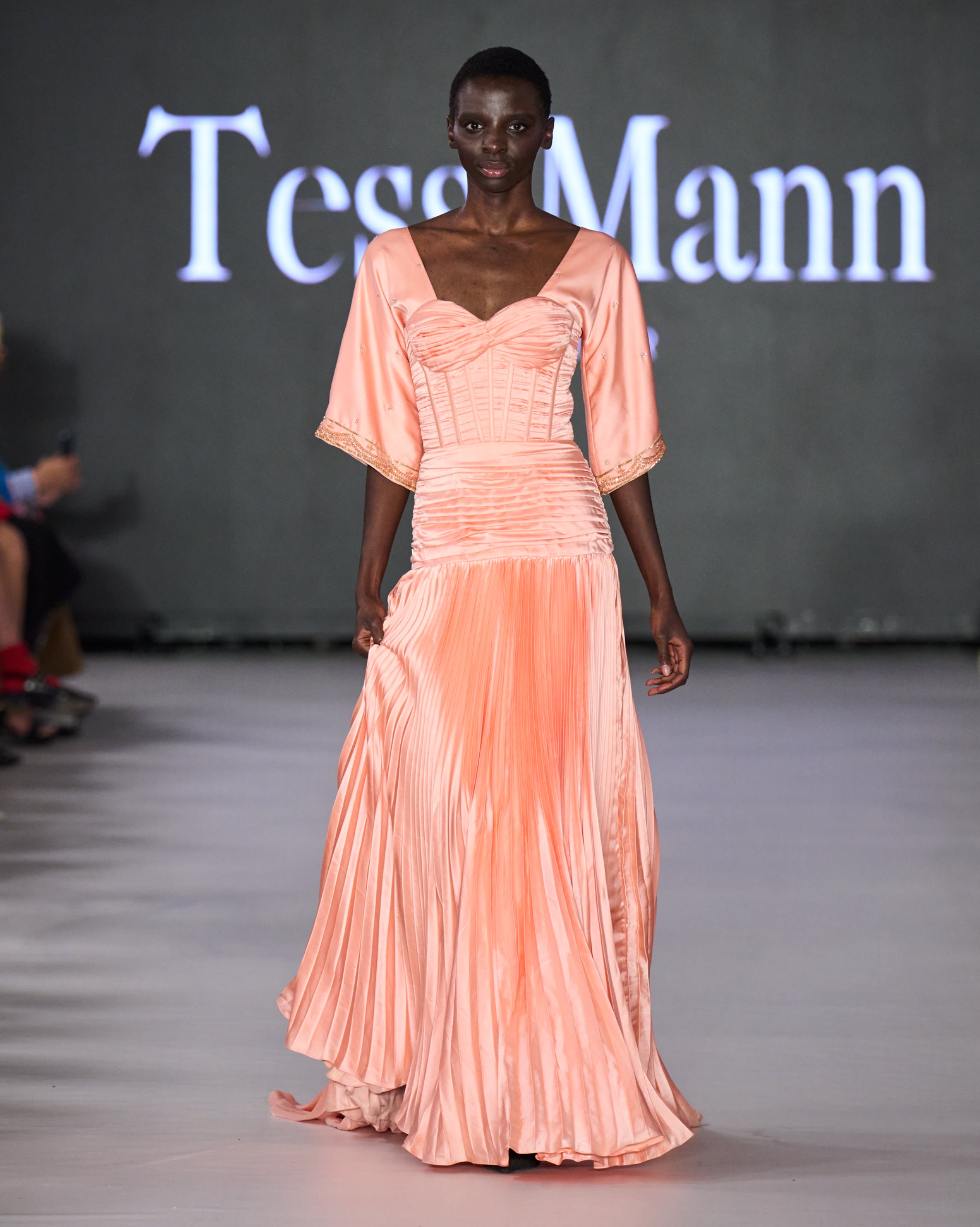 A model walking the runway wearing a long orange dress.