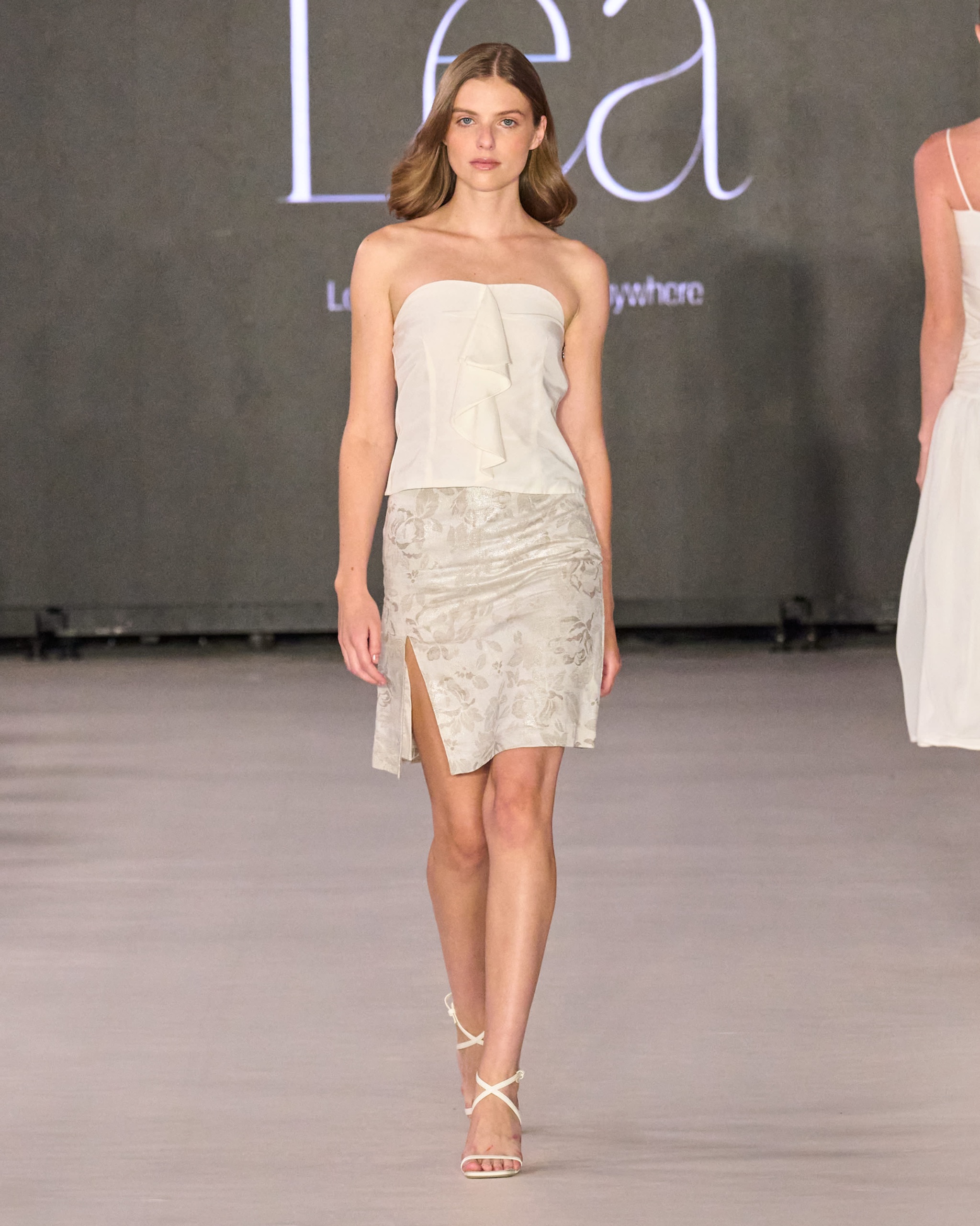 A model walking the runway wearing a white top and skirt.