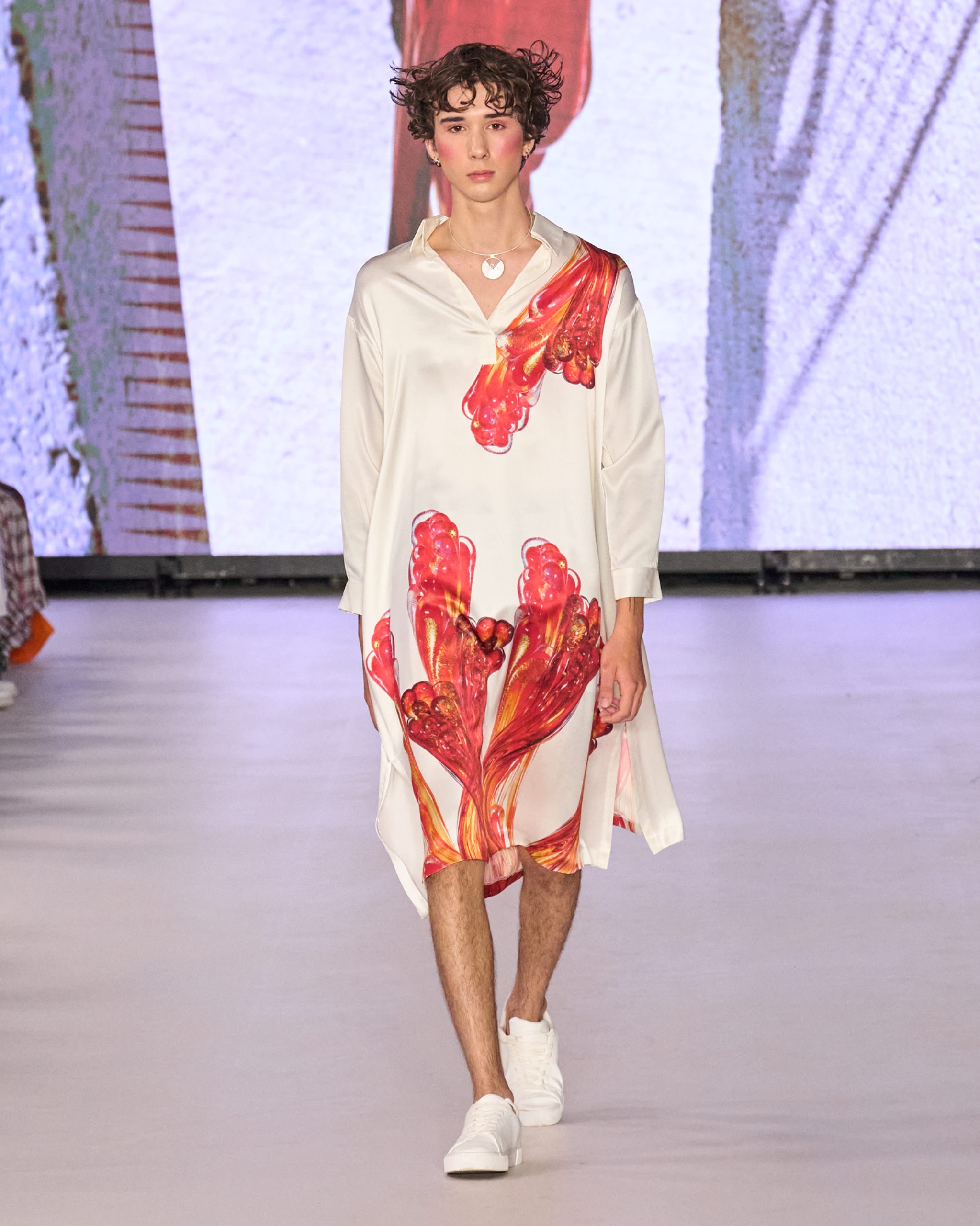 A model walking the runway wearing a white dress with orange detailing.