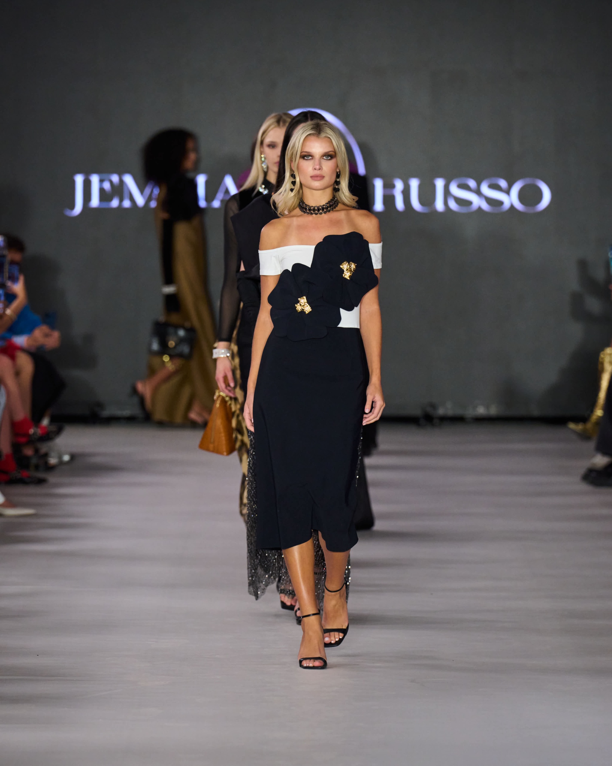 A model walking the runway wearing a black and white dress with black floral embellishments.