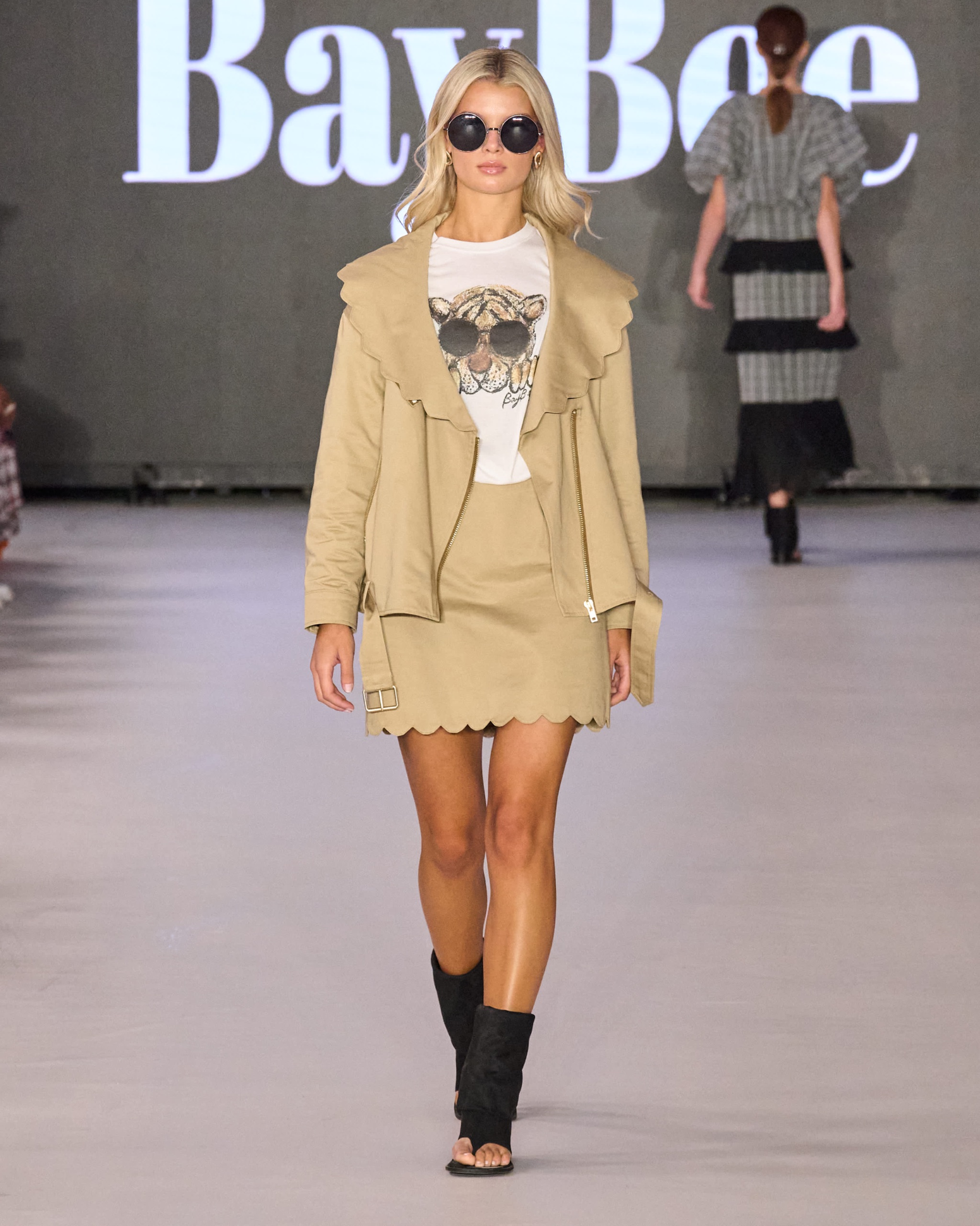 A model walking the runway wearing a beige blazer and skirt with a white t-shirt with an animal design.