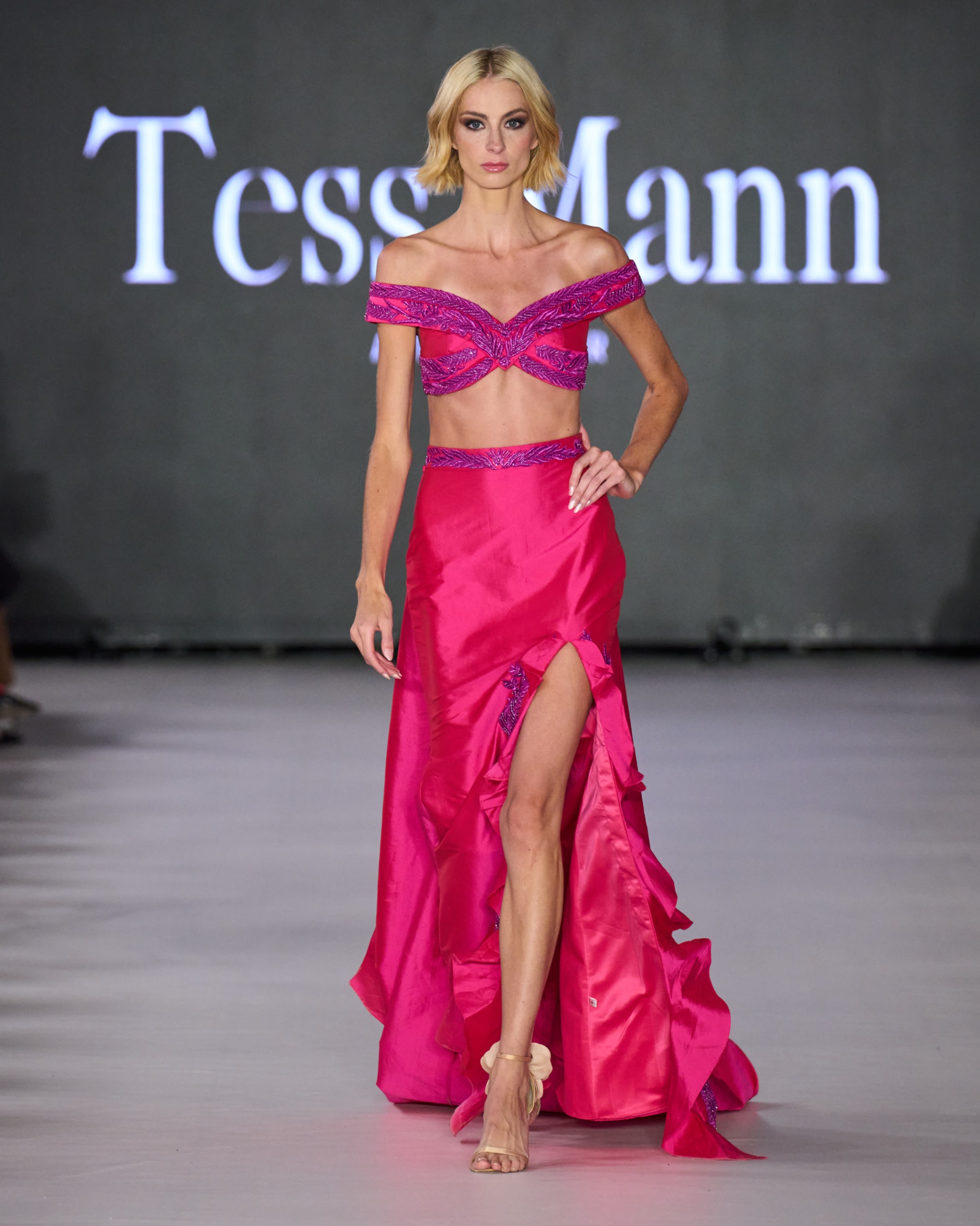 A model walking the runway wearing purple top with long pink skirt.