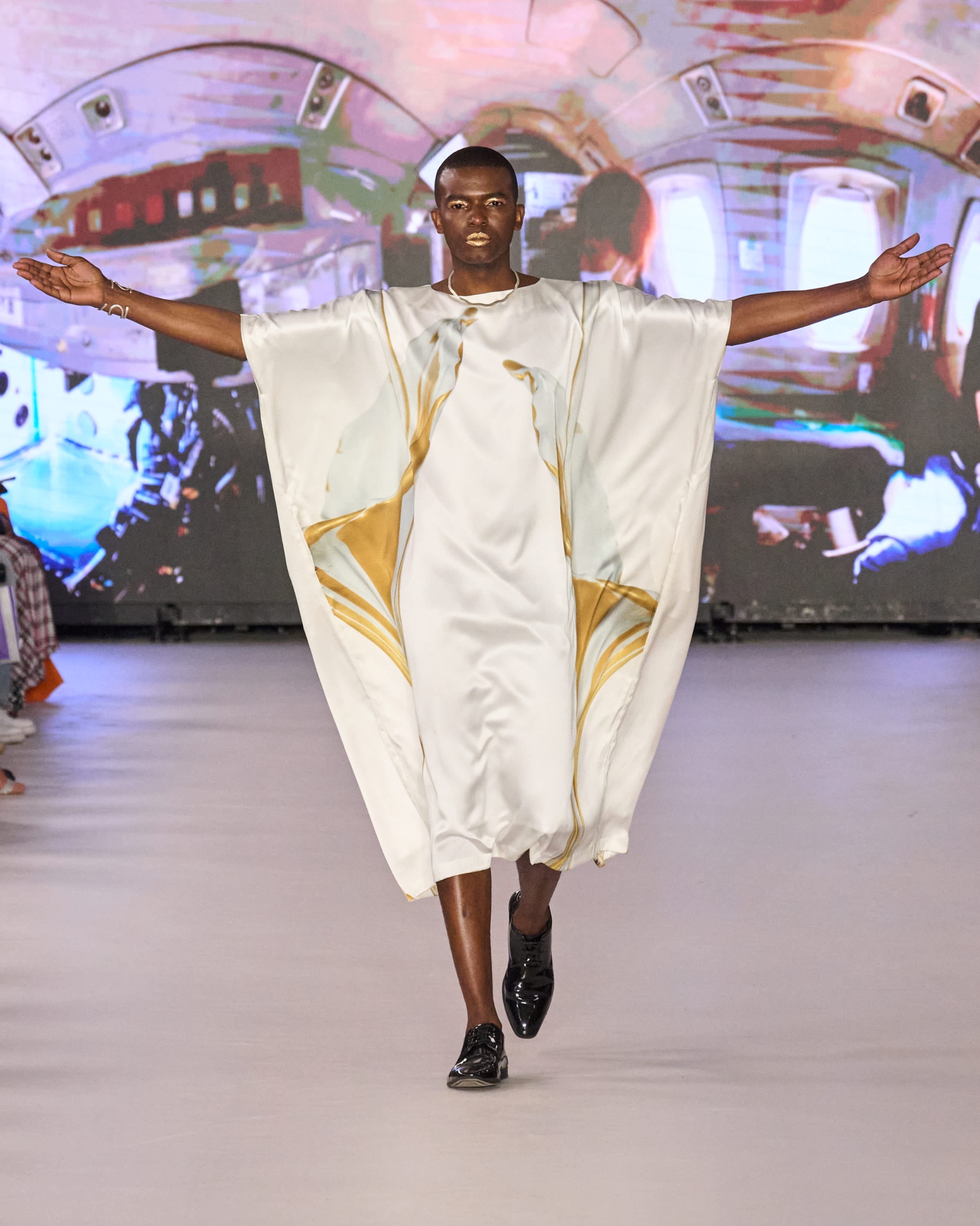 A model walking the runway wearing a white kimono-inspired robe with gold detailing.