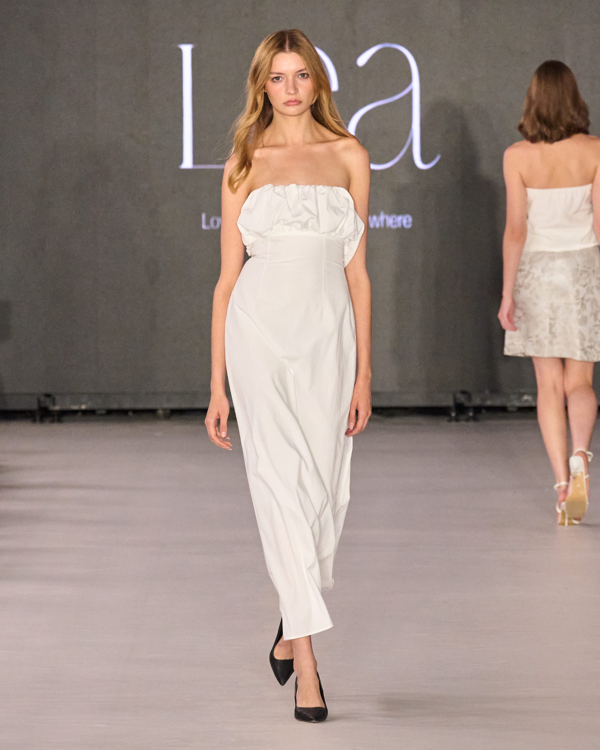 A model walking the runway wearing a white jumpsuit.