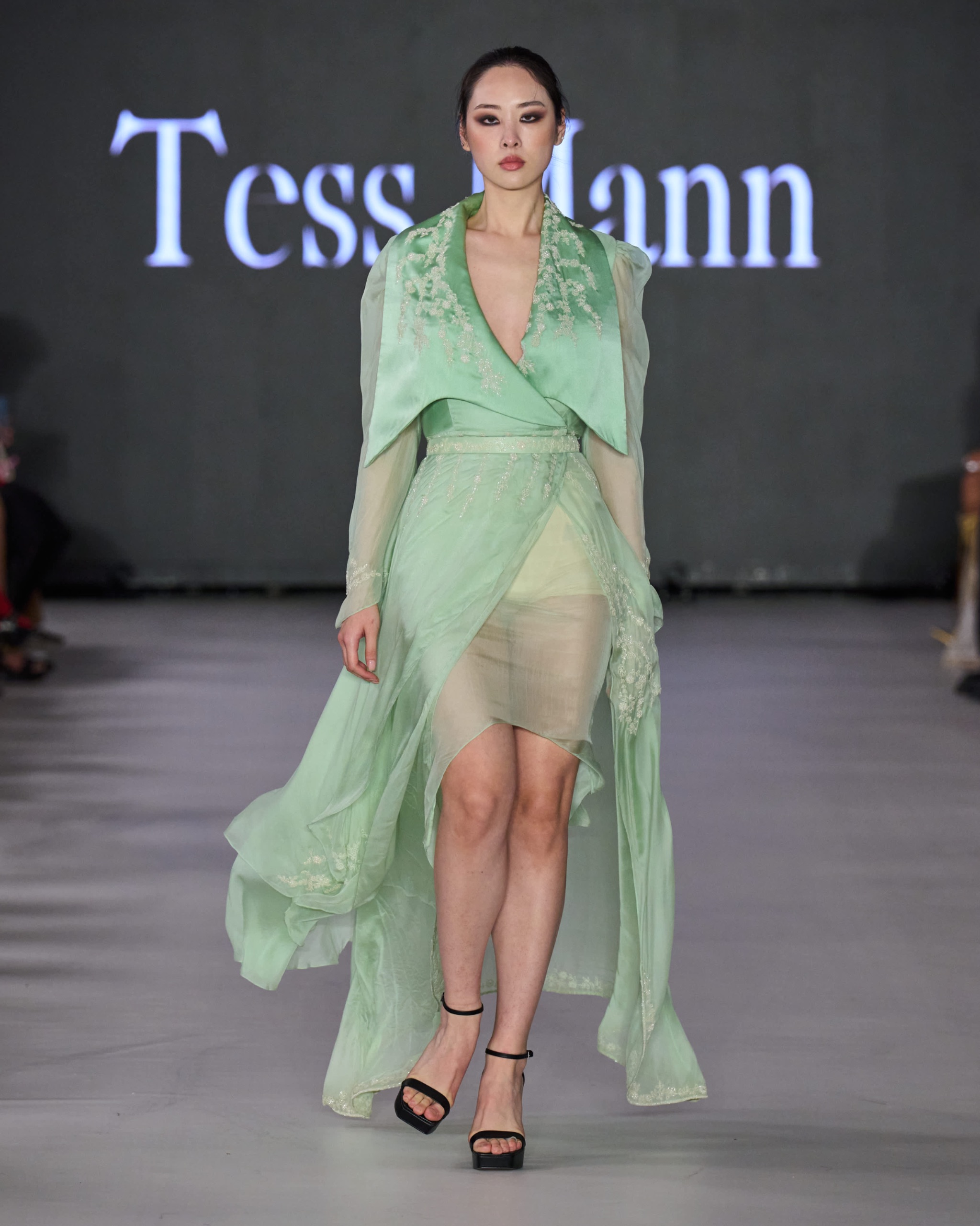 A model walking the runway wearing a green dress.