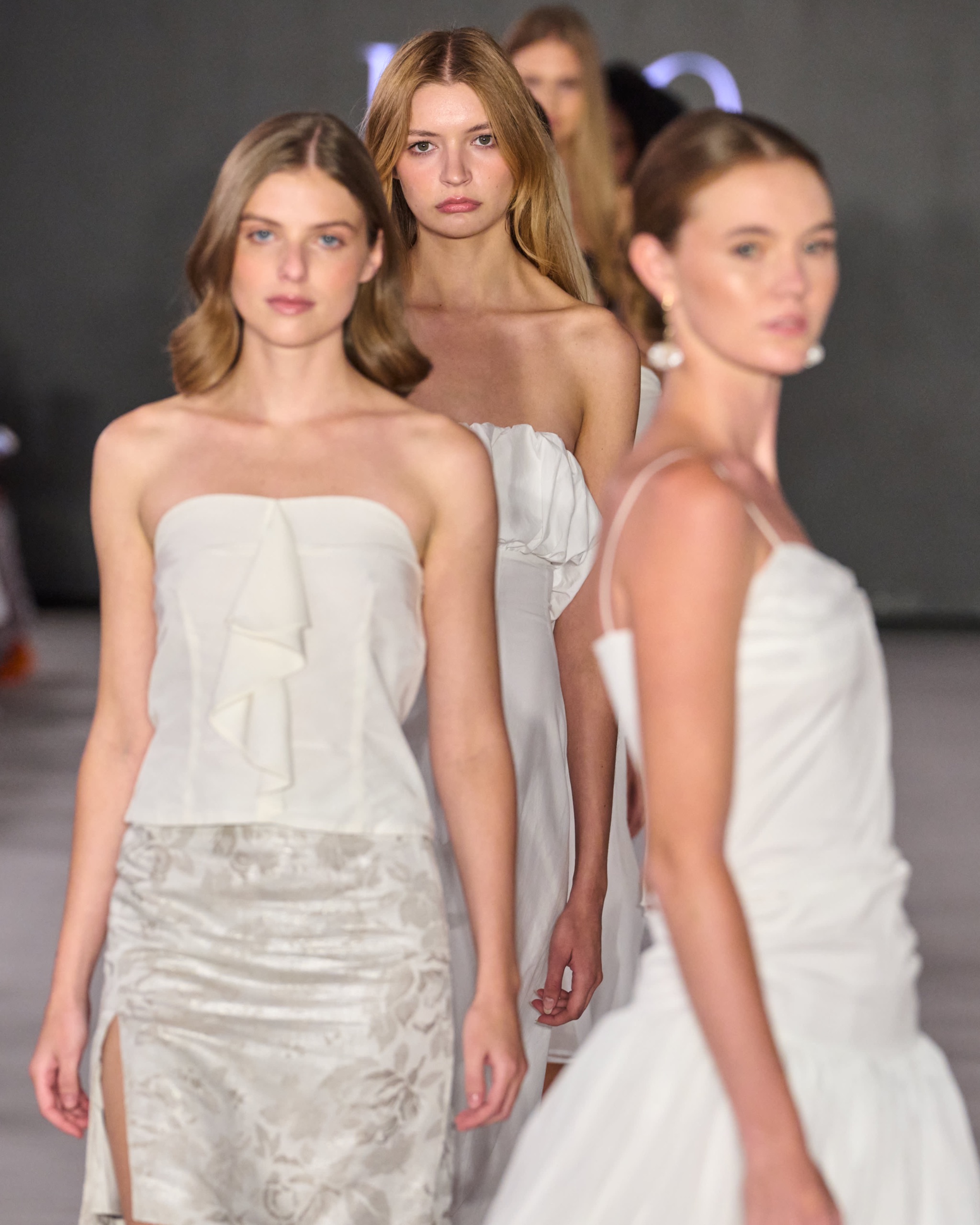 A photo of 4 models walking on the runway all wearing white outfits.