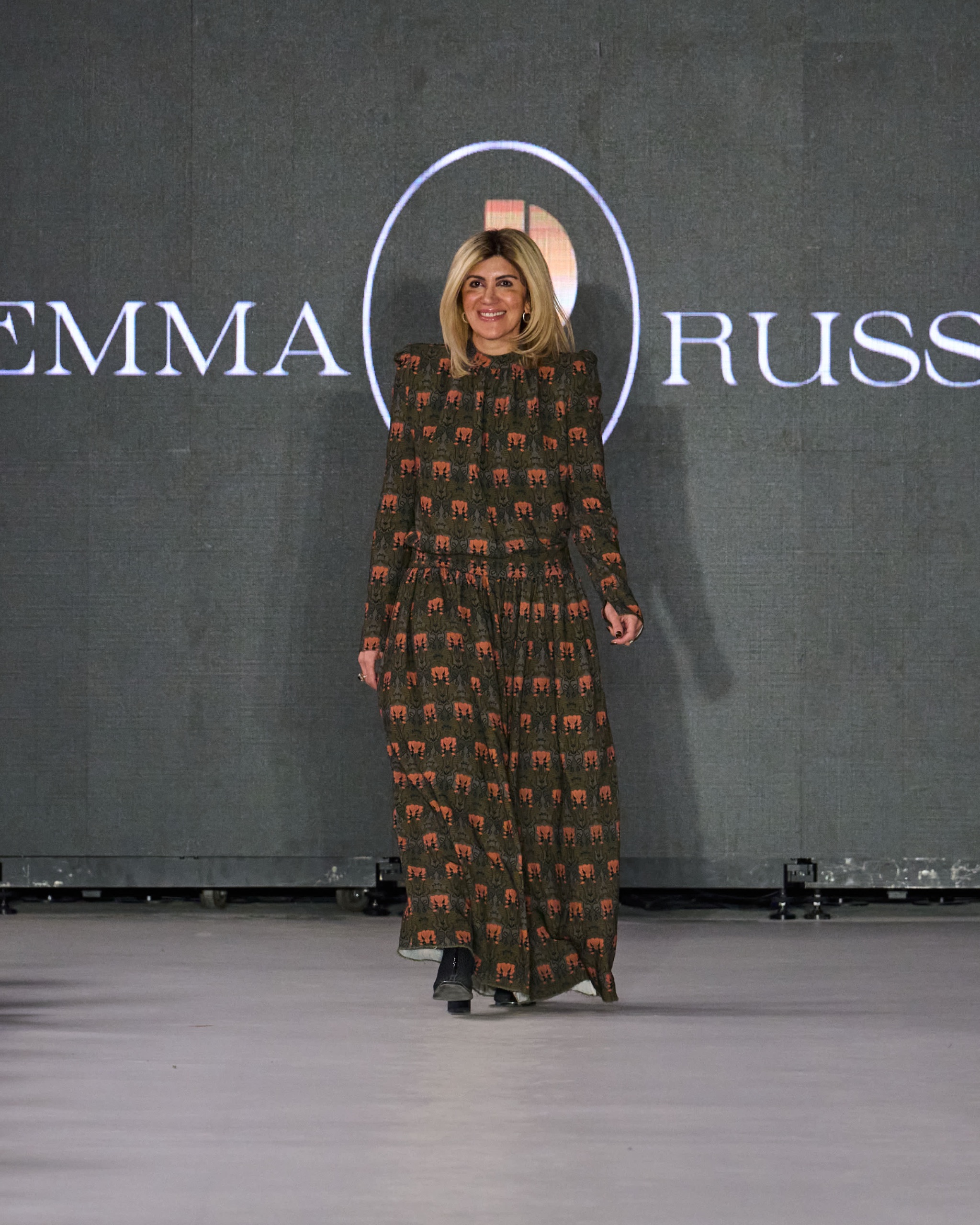 A model walking the runway wearing a long brown dress with a colourful pattern.