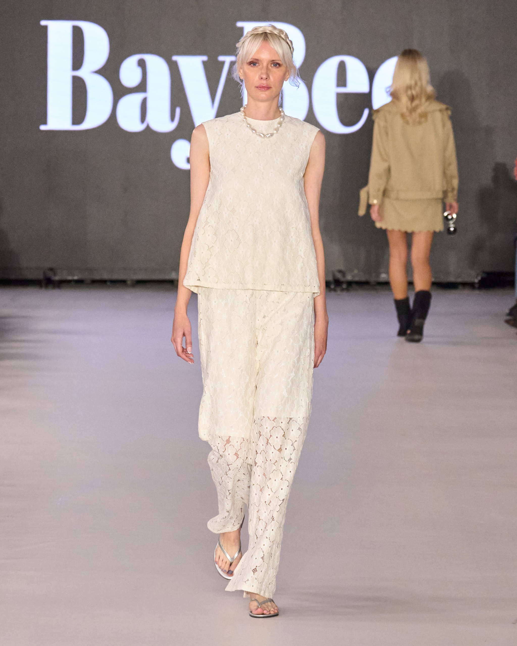 A model walking the runway wearing a white top and white trousers.